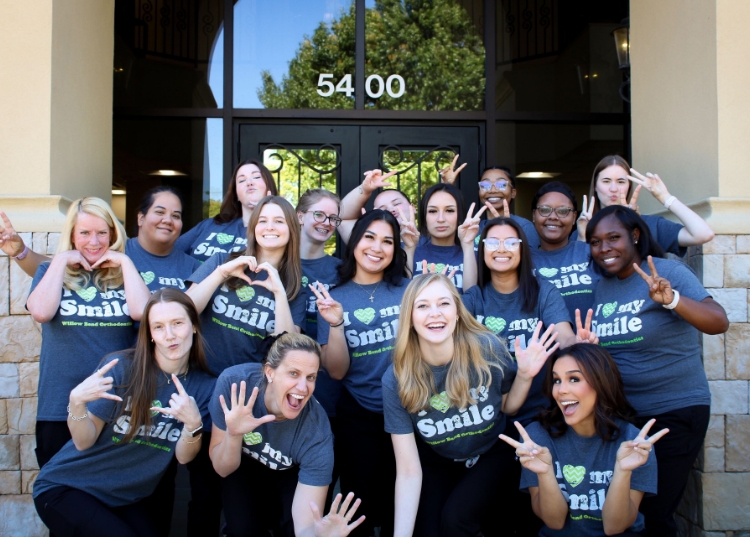 Dental team of over 15 people posing for group image in front of building