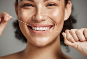 Smiling young woman flossing her teeth